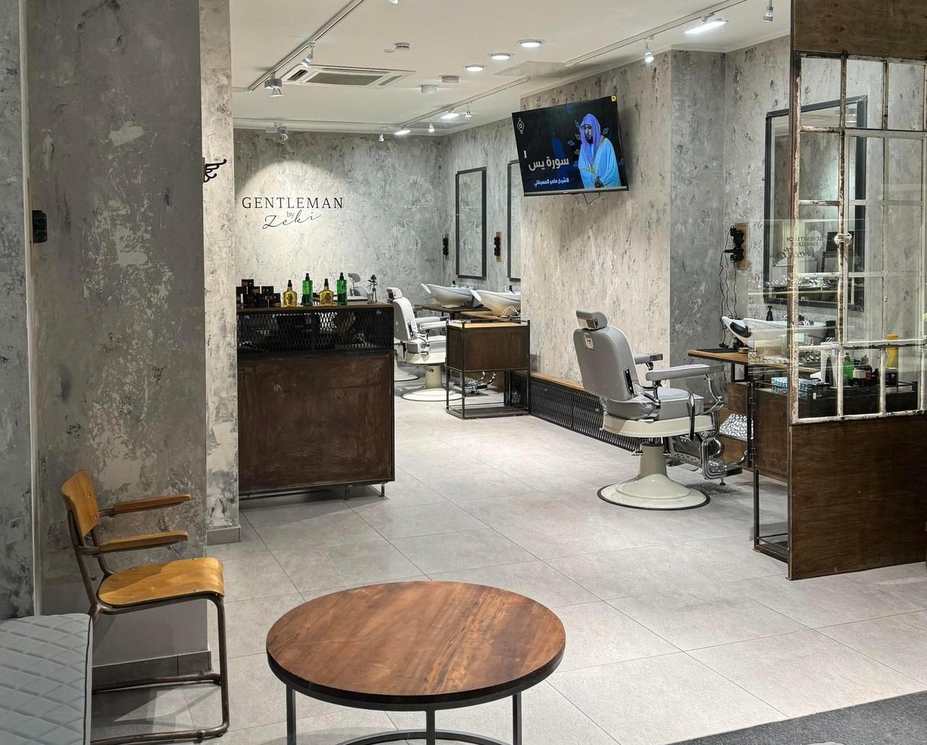 Der helle Innenraum des Barbierstudios mit Betonwänden, Barberstühlen und dunklen Holzelementen